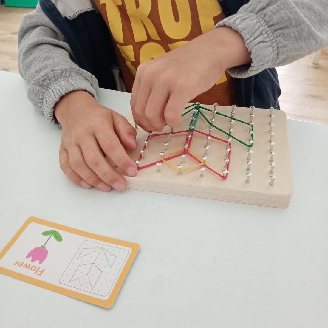 Deux mains tendent des élastiques de couleur sur un géoplan